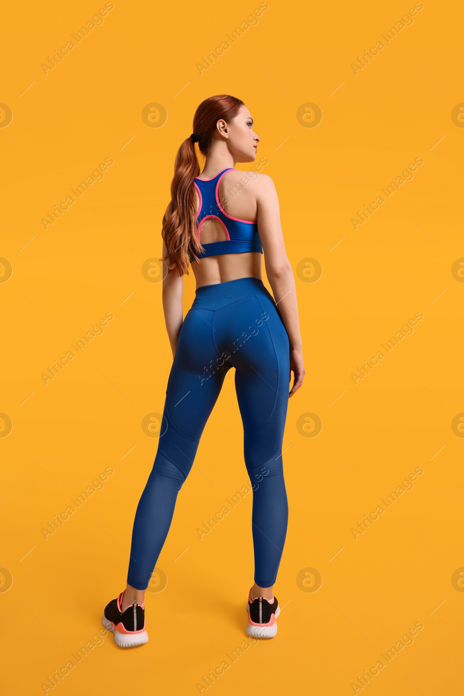 Photo of Young woman wearing sportswear on yellow background, back view