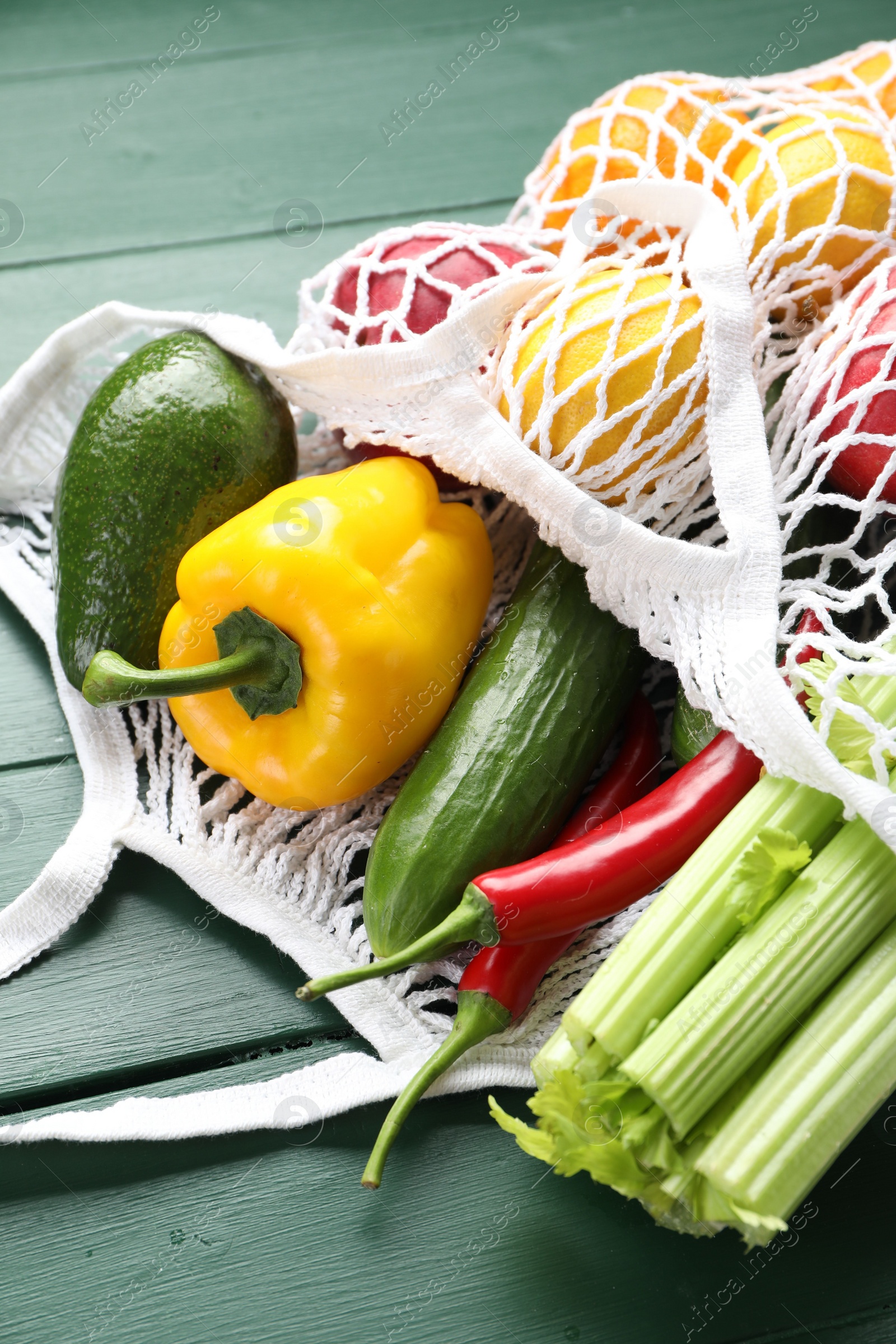Photo of String bag with different vegetables on green wooden table, closeup