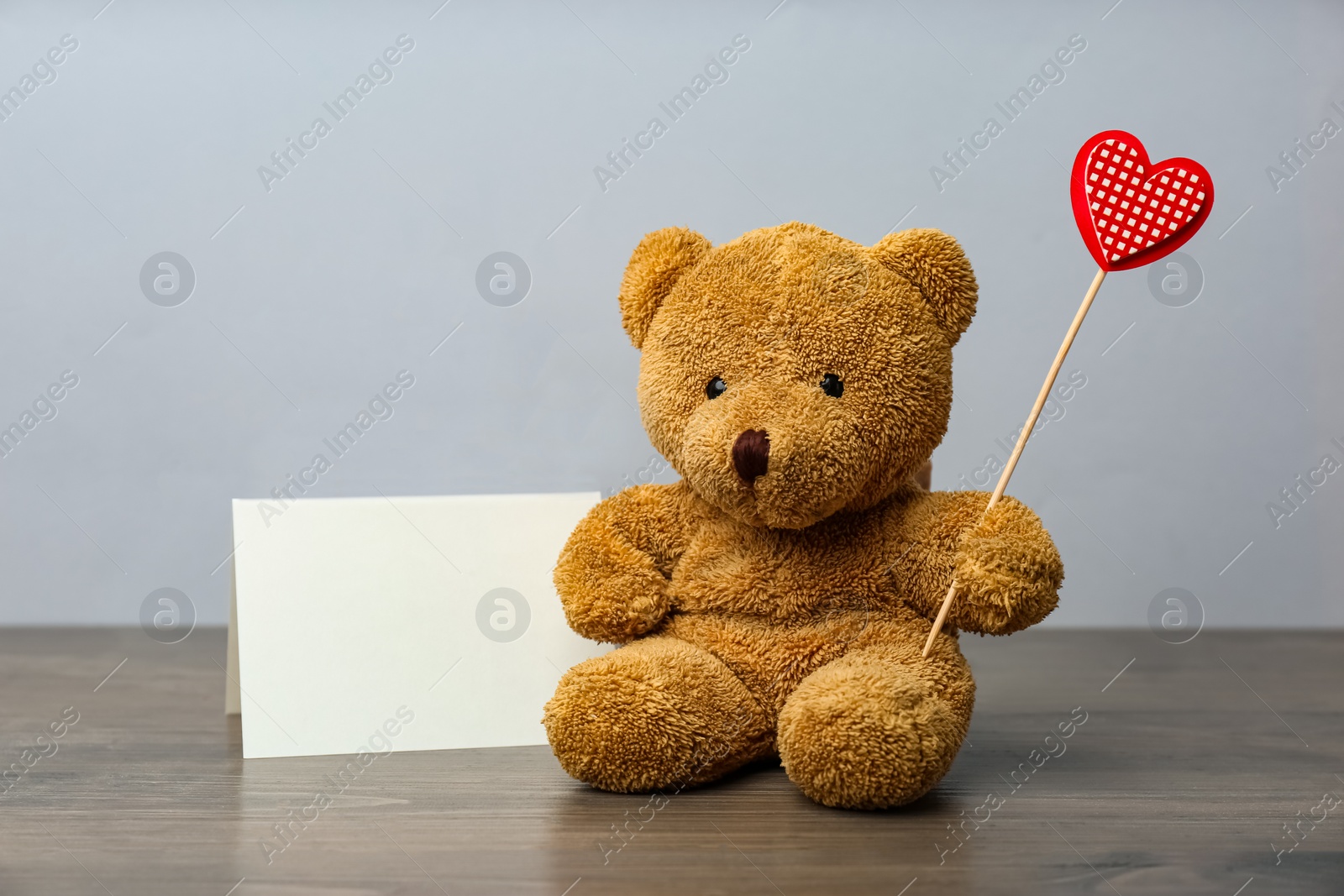 Photo of Cute teddy bear with red heart and blank card on wooden table. Valentine's day celebration