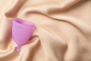 Menstrual cup on beige silk fabric, top view. Space for text