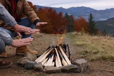 Photo of Men warming hands near bonfire outdoors, closeup. Camping season