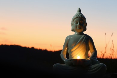 Photo of Decorative Buddha statue with burning candle outdoors at sunset. Space for text