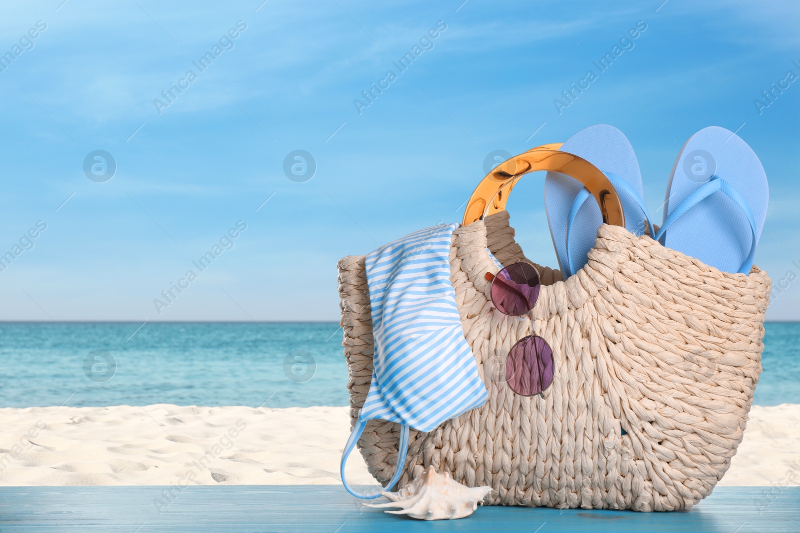 Image of Bag with bikini and accessories on sunny ocean beach, space for text. Summer vacation