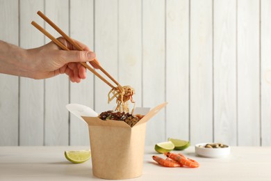 Photo of Woman eating seafood wok noodles with chopsticks from box at white wooden table, closeup. Space for text