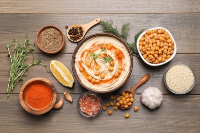 Photo of Delicious hummus with chickpeas and different ingredients on wooden table, flat lay