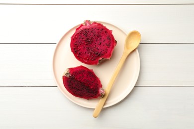 Photo of Plate with delicious cut red pitahaya fruit and spoon on white wooden table, top view
