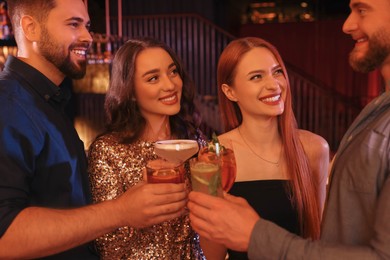 Photo of Happy friends clinking glasses with fresh cocktails in bar