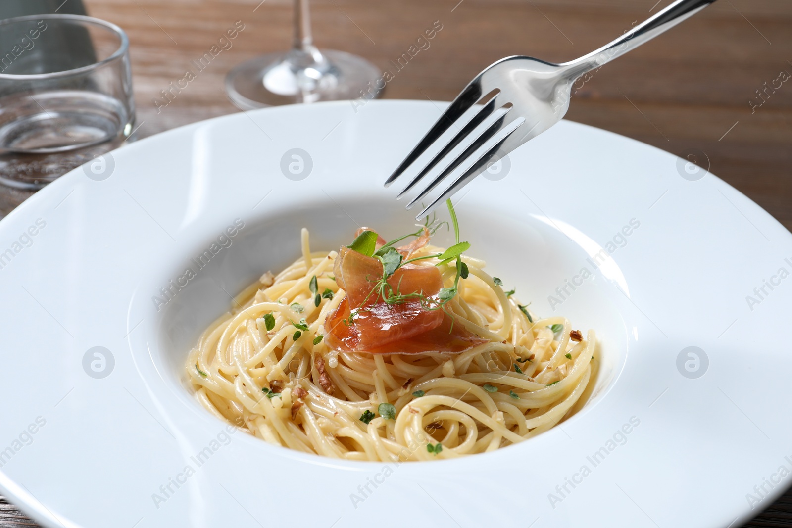 Photo of Eating tasty spaghetti with prosciutto and microgreens at table, closeup. Exquisite presentation of pasta dish