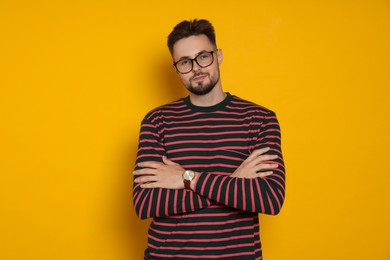 Handsome man in striped sweatshirt and eyeglasses on yellow background