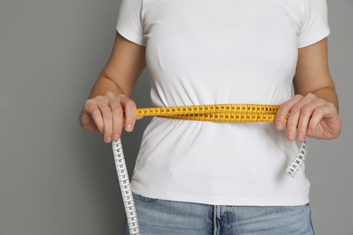 Woman measuring waist with tape on grey background, closeup