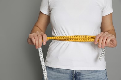 Photo of Woman measuring waist with tape on grey background, closeup