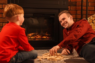 Photo of Happy father and son playing together on floor near fireplace at home