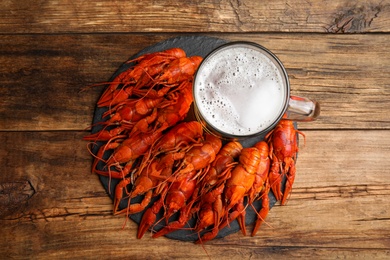 Delicious red boiled crayfishes and mug of beer on wooden table, top view