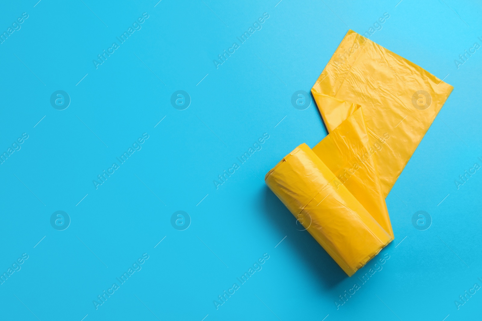 Photo of Roll of garbage bags on light blue background, top view. Space for text