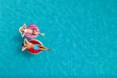 Happy couple with inflatable rings in swimming pool, top view and space for text. Summer vacation