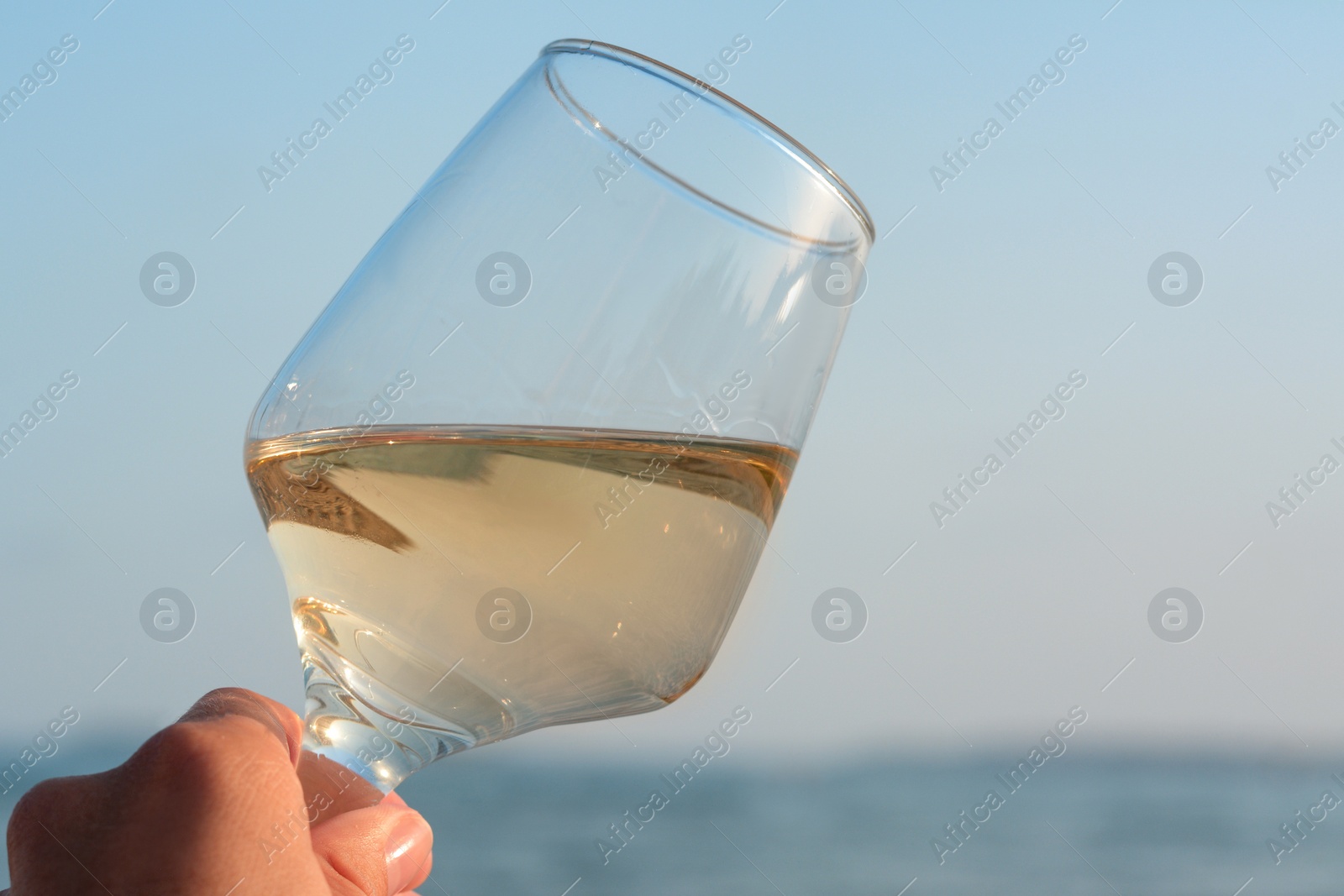 Photo of Woman holding glass of tasty wine near sea, closeup. Space for text