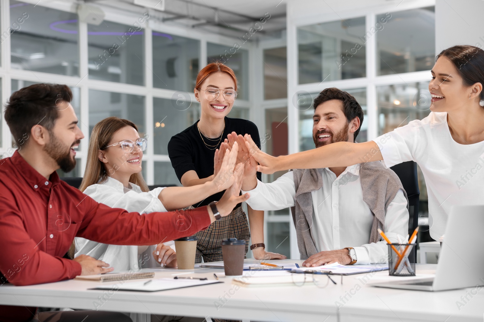 Photo of Team of employees joining hands in office