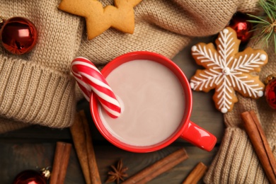 Photo of Flat lay composition with cup of tasty cocoa and Christmas candy cane on wooden table, flat lay