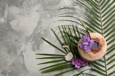 Photo of Young peeled coconut with straw, tropical leaf and flowers on grey table, flat lay. Space for text