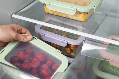 Woman taking box with frozen strawberry from refrigerator, closeup