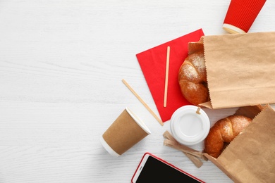 Photo of Flat lay composition with paper bags and pastry on light wooden background. Space for design