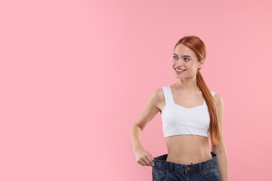 Photo of Slim woman wearing big jeans on pink background, space for text. Weight loss