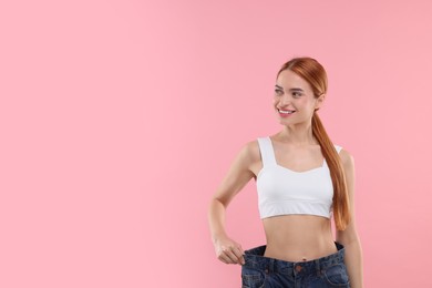 Slim woman wearing big jeans on pink background, space for text. Weight loss