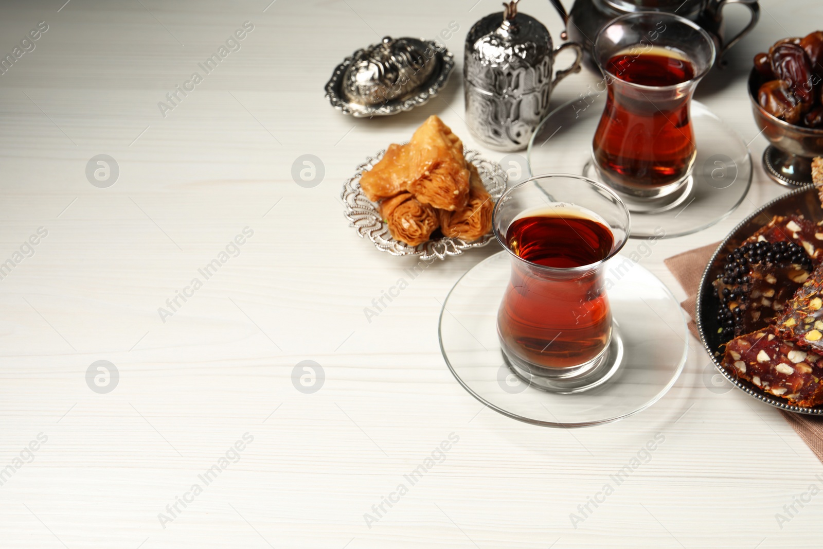 Photo of Glasses of tea, baklava dessert, Turkish delight and date fruits served in vintage tea set on white wooden table, space for text