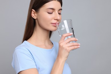 Healthy habit. Woman drinking fresh water from glass on grey background