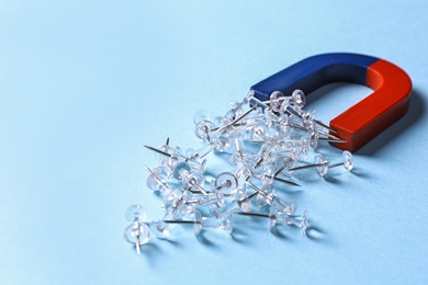 Photo of Red and blue horseshoe magnet attracting push pins on light blue background