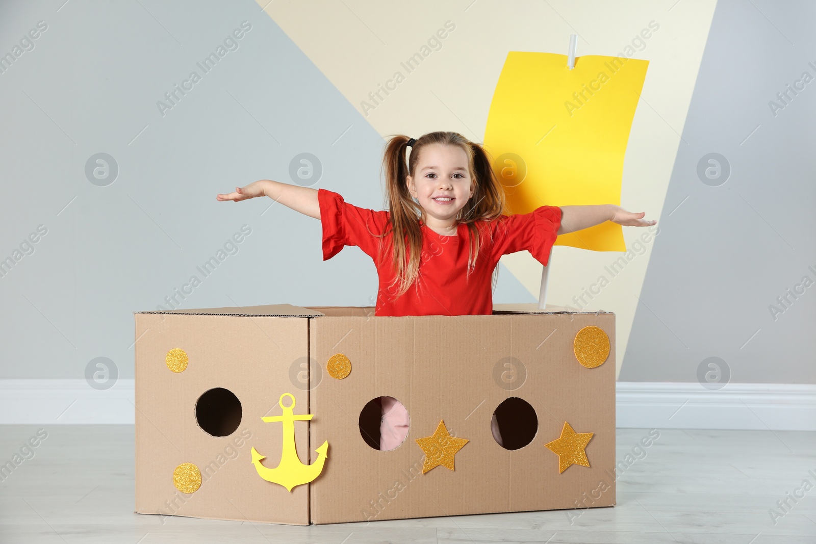 Photo of Cute little child playing with cardboard ship near color wall