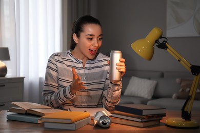 Photo of Emotional young woman with energy drink studying at home