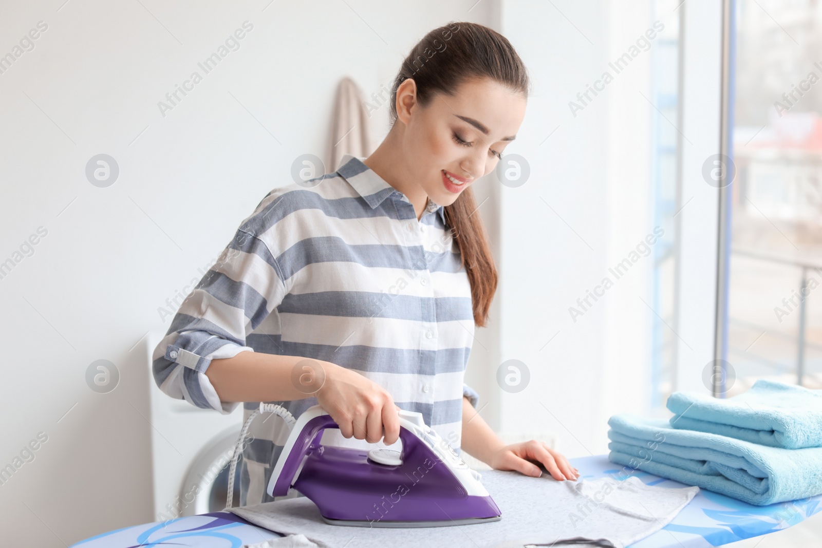 Photo of Young woman ironing clothes at home