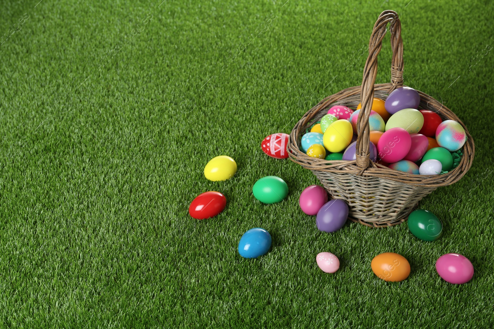 Photo of Wicker basket with Easter eggs on green grass. Space for text