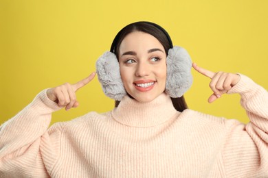 Photo of Beautiful young woman wearing earmuffs on yellow background