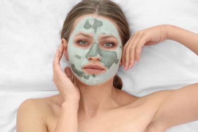 Photo of Beautiful woman with clay facial mask on white fabric, above view
