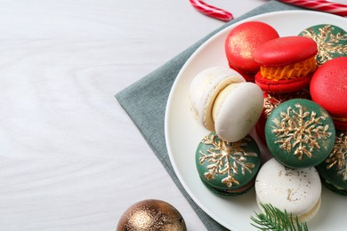 Photo of Different decorated Christmas macarons and festive decor on white wooden table. Space for text