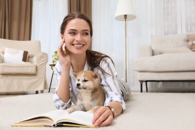 Happy young woman reading book with cute dog on floor in living room