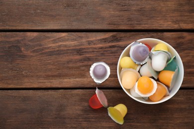 Bowl with tasty bright jelly cups on wooden table, flat lay. Space for text