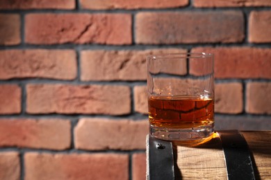 Photo of Glass of whiskey on wooden barrel against brick wall, closeup. Space for text