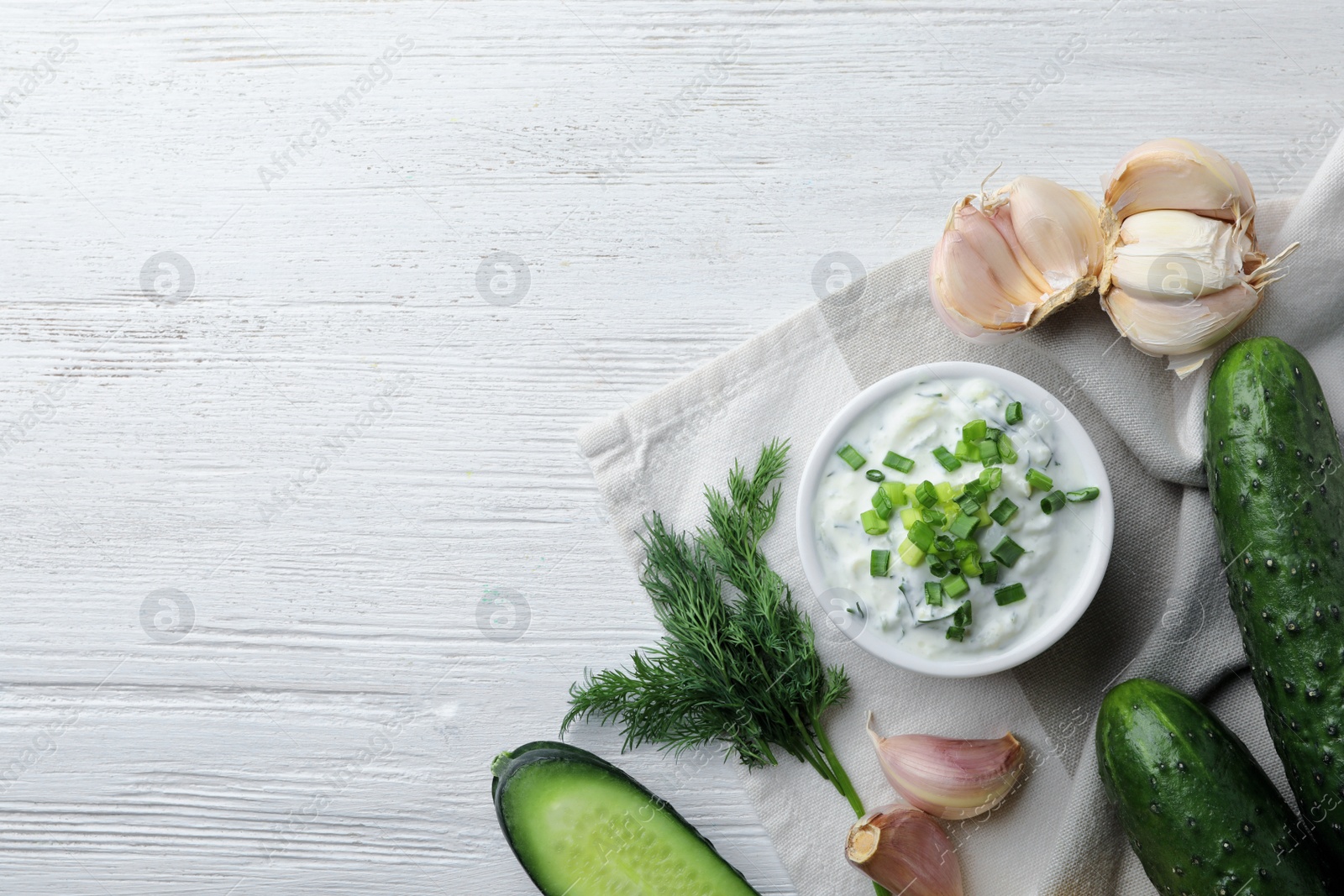 Photo of Tzatziki cucumber sauce with ingredients on wooden background, top view. Space for text