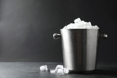 Photo of Metal bucket with ice cubes on table. Space for text