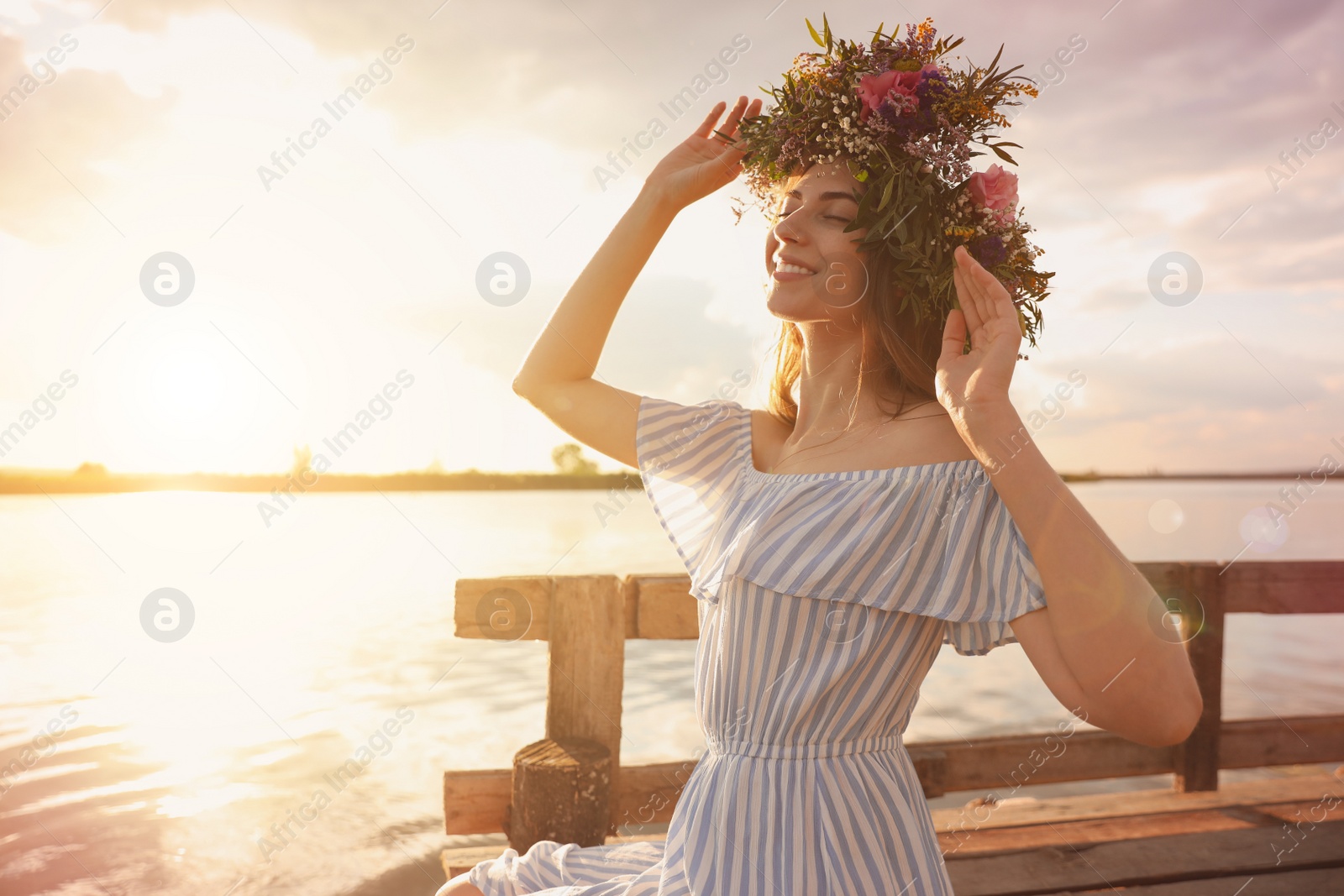Photo of Young woman wearing wreath made of beautiful flowers on pier near river