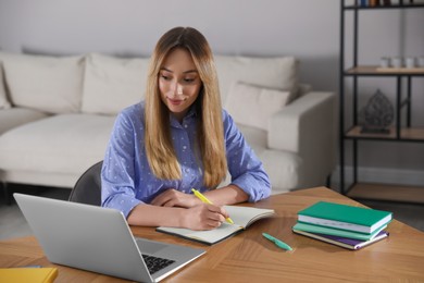 Young woman writing down notes during webinar at table in room