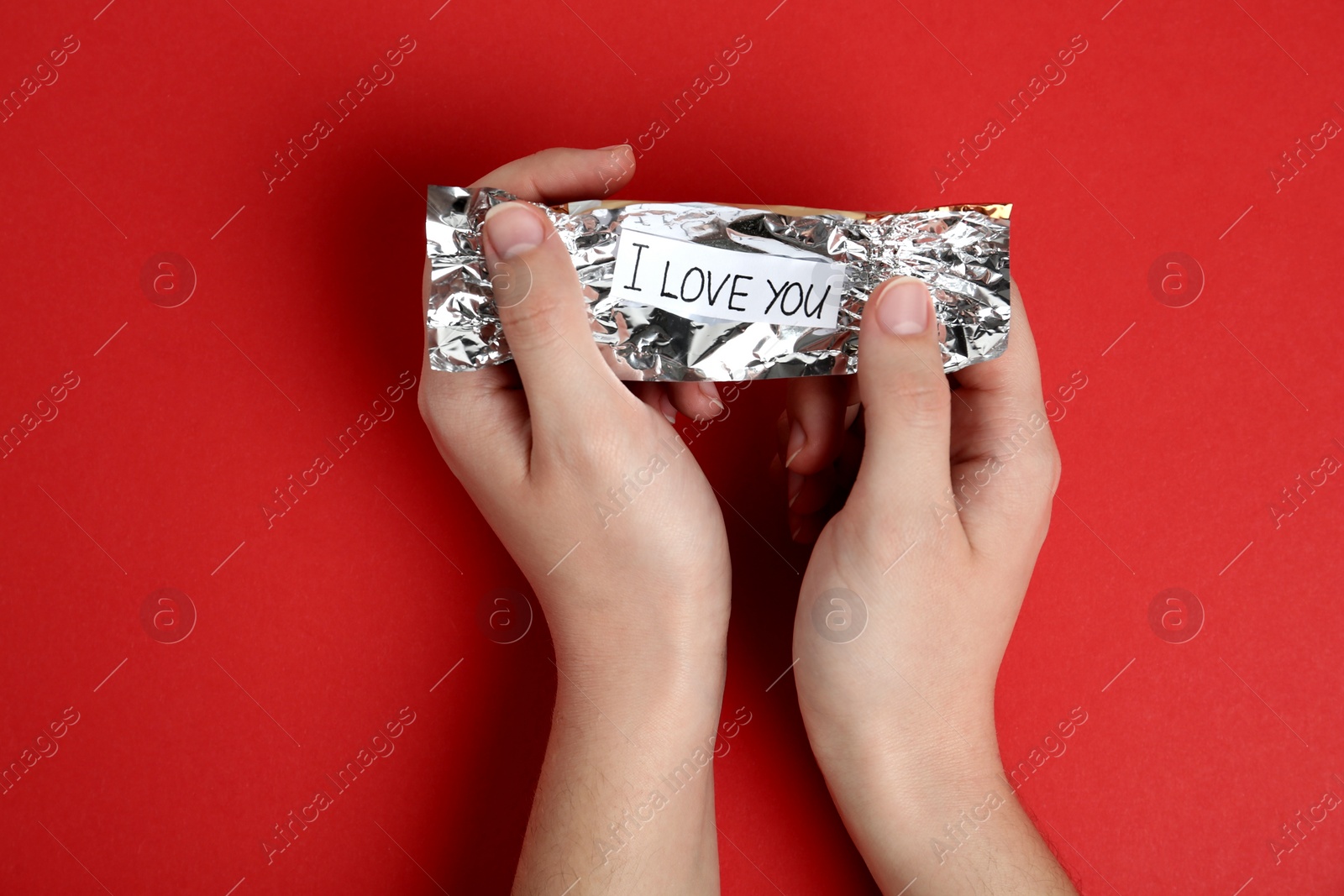 Photo of Woman holding candy wrapper with message I Love You on red background, top view