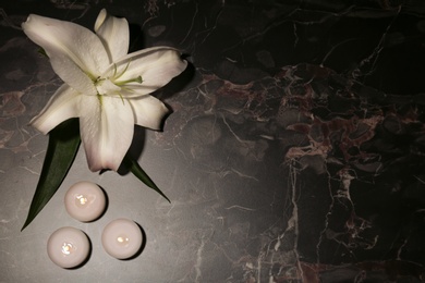 Photo of Beautiful lily with burning candles and space for text on dark marble background. Funeral flower