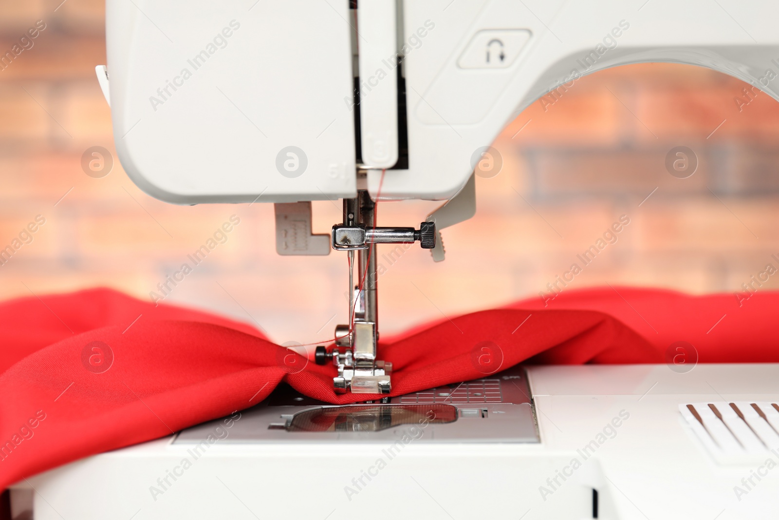 Photo of Sewing machine with red fabric indoors, closeup