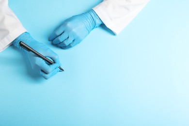Photo of Doctor wearing medical gloves writing something on light blue background, top view. Space for text