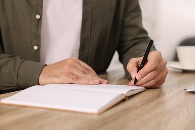 Photo of Young man writing in notebook at wooden table, closeup