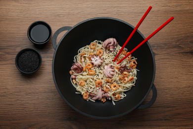 Stir fried noodles with seafood in wok on wooden table, flat lay